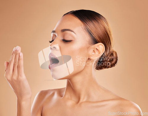 Image of Beauty, hygiene and bad breath with a model woman in studio on a brown background breathing into her hand. Skincare, dentist and face with an attractive young female smelling her mouth for freshness