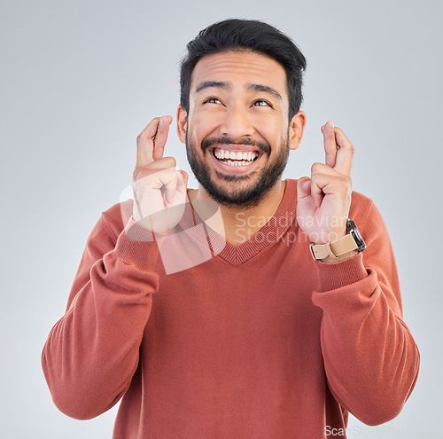 Image of Thinking, luck and hand gesture with a man in studio on a gray background praying in hope of a miracle. Idea, smile and fingers crossed with a happy or handsome young male wishing for good fortune