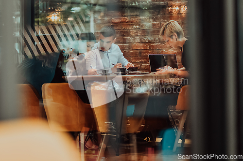 Image of Photo through the glass of a group of business people sitting in a cafe and discussing business plans and ideas for new online commercial services