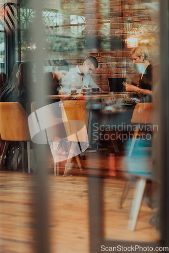 Image of Photo through the glass of a group of business people sitting in a cafe and discussing business plans and ideas for new online commercial services