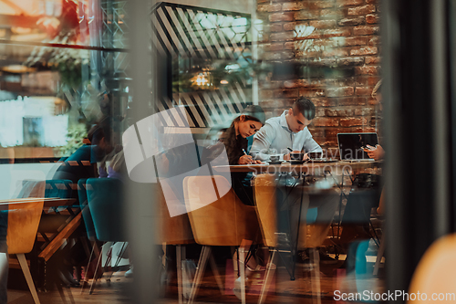 Image of Photo through the glass of a group of business people sitting in a cafe and discussing business plans and ideas for new online commercial services