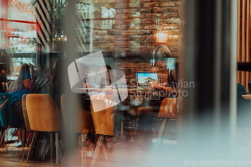 Image of Photo through the glass of a group of business people sitting in a cafe and discussing business plans and ideas for new online commercial services