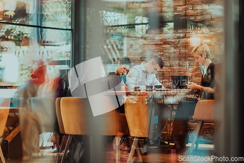 Image of Photo through the glass of a group of business people sitting in a cafe and discussing business plans and ideas for new online commercial services