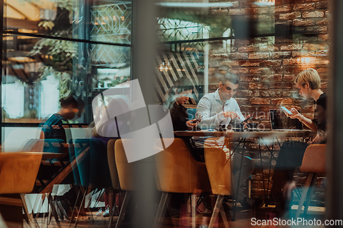 Image of Photo through the glass of a group of business people sitting in a cafe and discussing business plans and ideas for new online commercial services