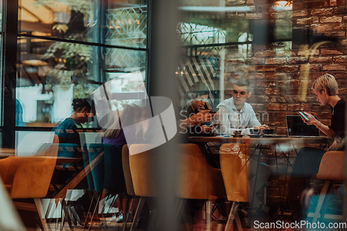 Image of Photo through the glass of a group of business people sitting in a cafe and discussing business plans and ideas for new online commercial services