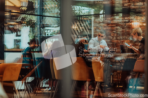 Image of Photo through the glass of a group of business people sitting in a cafe and discussing business plans and ideas for new online commercial services