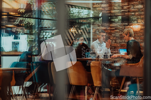 Image of Photo through the glass of a group of business people sitting in a cafe and discussing business plans and ideas for new online commercial services