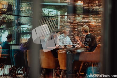 Image of Photo through the glass of a group of business people sitting in a cafe and discussing business plans and ideas for new online commercial services