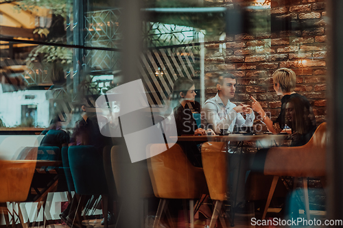 Image of Photo through the glass of a group of business people sitting in a cafe and discussing business plans and ideas for new online commercial services