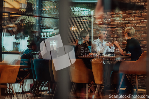 Image of Photo through the glass of a group of business people sitting in a cafe and discussing business plans and ideas for new online commercial services