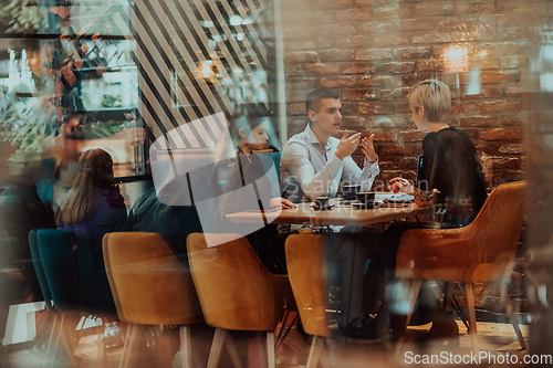 Image of Photo through the glass of a group of business people sitting in a cafe and discussing business plans and ideas for new online commercial services