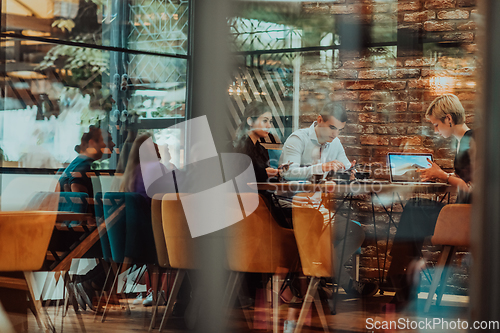 Image of Photo through the glass of a group of business people sitting in a cafe and discussing business plans and ideas for new online commercial services