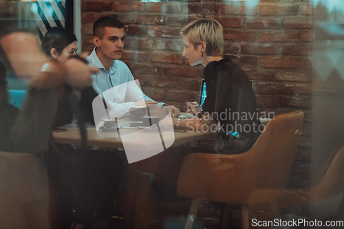 Image of Photo through the glass of a group of business people sitting in a cafe and discussing business plans and ideas for new online commercial services