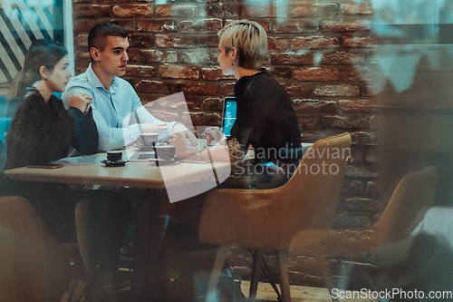 Image of Photo through the glass of a group of business people sitting in a cafe and discussing business plans and ideas for new online commercial services