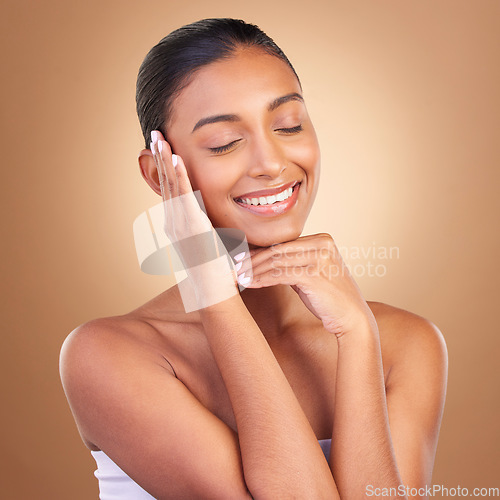 Image of Beauty, skincare and happy with indian woman and touch in studio for happy, spa and facial. Cosmetics, self care and glow with model on brown background for satisfaction, makeup and confidence