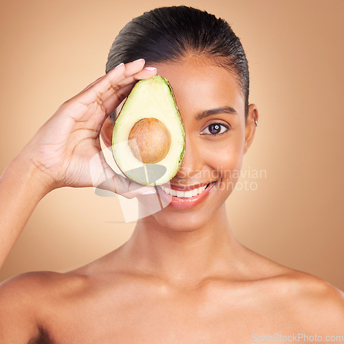 Image of Indian woman, avocado and studio portrait for beauty, health and wellness with fruit by brown background. Asian young model and girl with organic self care with fruits, healthy cosmetic and skin glow