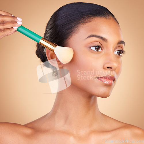 Image of Makeup, cheek and brush with indian woman in studio for foundation, blush and self care. Glow, cosmetics and facial with female model isolated on brown background for shine, clean and confidence