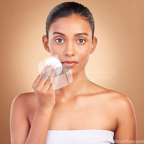 Image of Beauty, serious and cotton with portrait of indian woman in studio for self care, makeup remover and cosmetics. Skincare, clean and glow with model on brown background for results, natural and facial