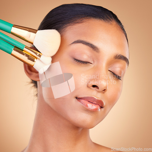 Image of Makeup, relax and brush with indian woman in studio for foundation, blush and self care. Glow, cosmetics and facial with female model isolated on brown background for shine, clean and confidence