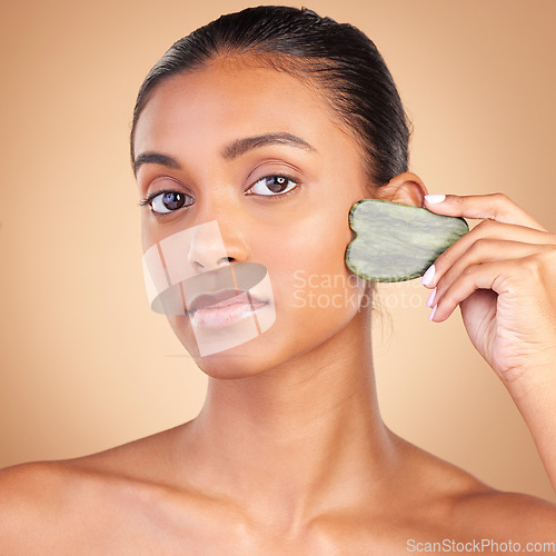 Image of Beauty, gua sha and portrait of Indian woman for skincare, facial treatment and wellness with spa tools. Salon, dermatology and girl on brown background with cosmetics, face massage and luxury stone