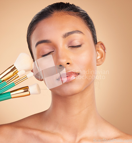 Image of Makeup, beauty and brush with indian woman in studio for foundation, blush and self care. Glow, cosmetics and facial with female model isolated on brown background for shine, clean and confidence