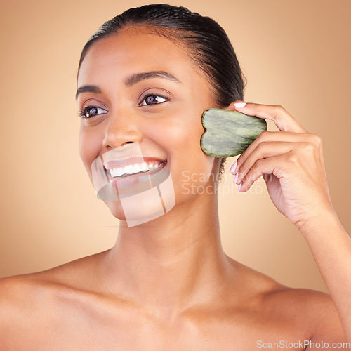 Image of Beauty, gua sha and face of Indian woman for skincare, facial treatment and wellness with spa tools. Salon, dermatology and happy girl on brown background for cosmetics, face massage and luxury stone