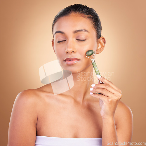 Image of Facial, massage and beauty with a model woman in studio on a brown background for natural antiaging skincare. Wellness, luxury and product with an attractive young female using a roller for skin lift