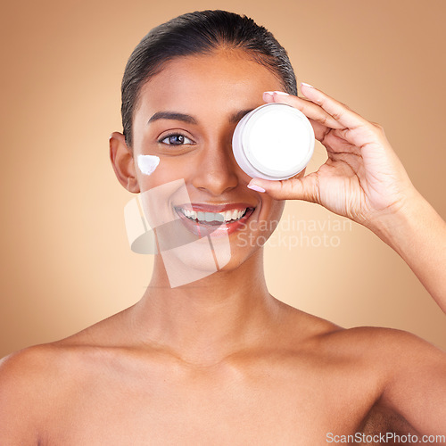 Image of Indian woman, skincare cream and jar in portrait with smile, happiness and wellness by brown background. Happy model, lotion product and face in studio for dermatology, aesthetic and cosmetic beauty