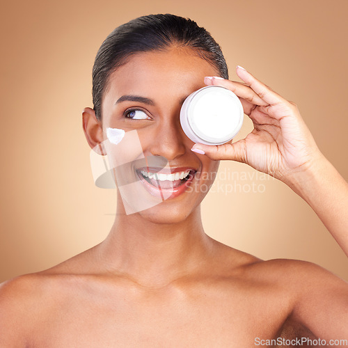 Image of Indian woman, skincare cream and jar in studio with smile, happiness and wellness by brown background. Happy model, lotion product and face with thinking, dermatology and young with cosmetic beauty