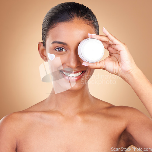 Image of Indian woman, skin and cream jar in portrait with smile, happiness and wellness by brown background. Happy model, lotion product and skincare in studio for dermatology, healthy and cosmetic beauty