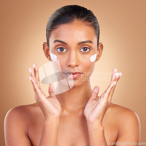 Image of Indian woman, skincare cream and hands in portrait with health, serious or wellness by brown background. Young model, lotion product or face with aesthetic, dermatology and clean with cosmetic beauty