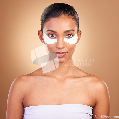 Image of Skincare, eye patch and portrait of Indian woman in studio for facial, spa treatment and glow. Self care, cosmetics and hydration with female model on brown background for mask, product and youth