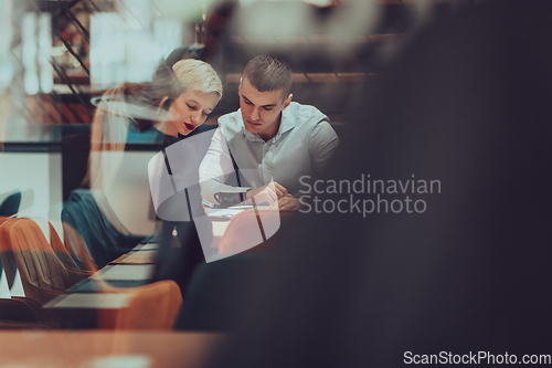 Image of Photo through the glass of a group of business people sitting in a cafe and discussing business plans and ideas for new online commercial services