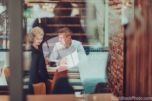 Image of Photo through the glass of a group of business people sitting in a cafe and discussing business plans and ideas for new online commercial services