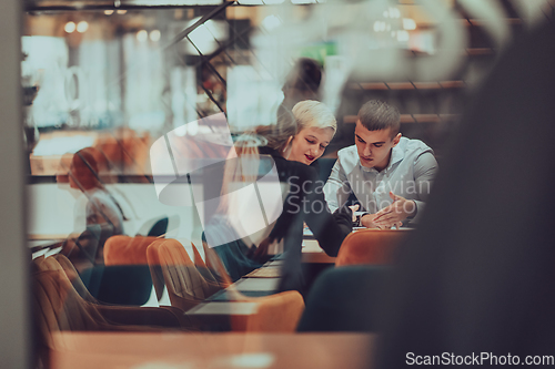 Image of Photo through the glass of a group of business people sitting in a cafe and discussing business plans and ideas for new online commercial services