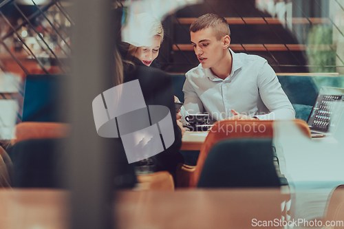 Image of Photo through the glass of a group of business people sitting in a cafe and discussing business plans and ideas for new online commercial services