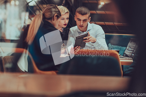 Image of Photo through the glass of a group of business people sitting in a cafe and discussing business plans and ideas for new online commercial services