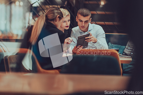 Image of Photo through the glass of a group of business people sitting in a cafe and discussing business plans and ideas for new online commercial services