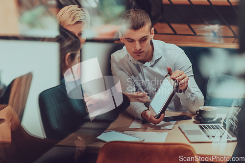 Image of Photo through the glass of a group of business people sitting in a cafe and discussing business plans and ideas for new online commercial services