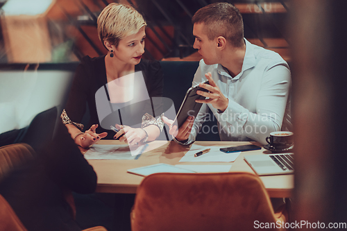 Image of Photo through the glass of a group of business people sitting in a cafe and discussing business plans and ideas for new online commercial services