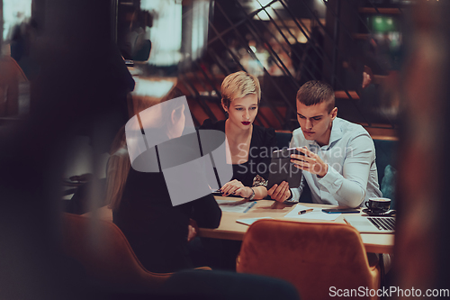 Image of Photo through the glass of a group of business people sitting in a cafe and discussing business plans and ideas for new online commercial services