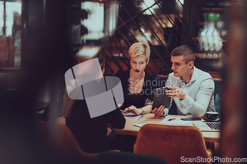 Image of Photo through the glass of a group of business people sitting in a cafe and discussing business plans and ideas for new online commercial services