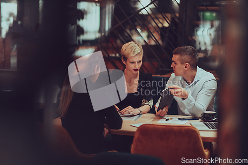 Image of Photo through the glass of a group of business people sitting in a cafe and discussing business plans and ideas for new online commercial services