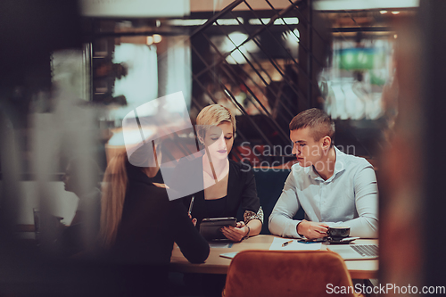 Image of Photo through the glass of a group of business people sitting in a cafe and discussing business plans and ideas for new online commercial services