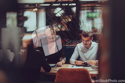 Image of Photo through the glass of a group of business people sitting in a cafe and discussing business plans and ideas for new online commercial services