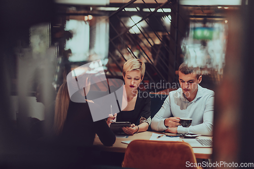 Image of Photo through the glass of a group of business people sitting in a cafe and discussing business plans and ideas for new online commercial services