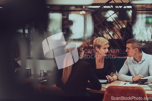 Image of Photo through the glass of a group of business people sitting in a cafe and discussing business plans and ideas for new online commercial services