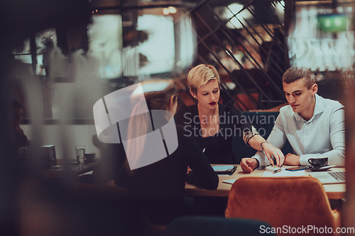 Image of Photo through the glass of a group of business people sitting in a cafe and discussing business plans and ideas for new online commercial services