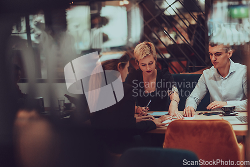 Image of Photo through the glass of a group of business people sitting in a cafe and discussing business plans and ideas for new online commercial services