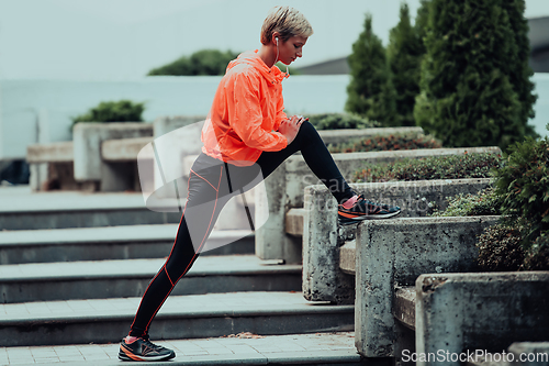 Image of Fit attractive woman in sportswear stretching one leg before jogging on the footpath outdoor in summer among greenery. Workout, sport, activity, fitness, vacation and training concept.